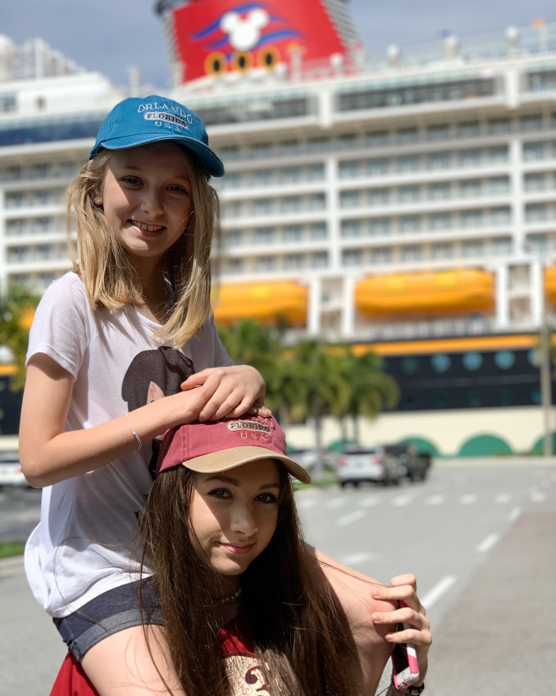 Two kids in Disney caps at the cruise port, the Disney ship behind them